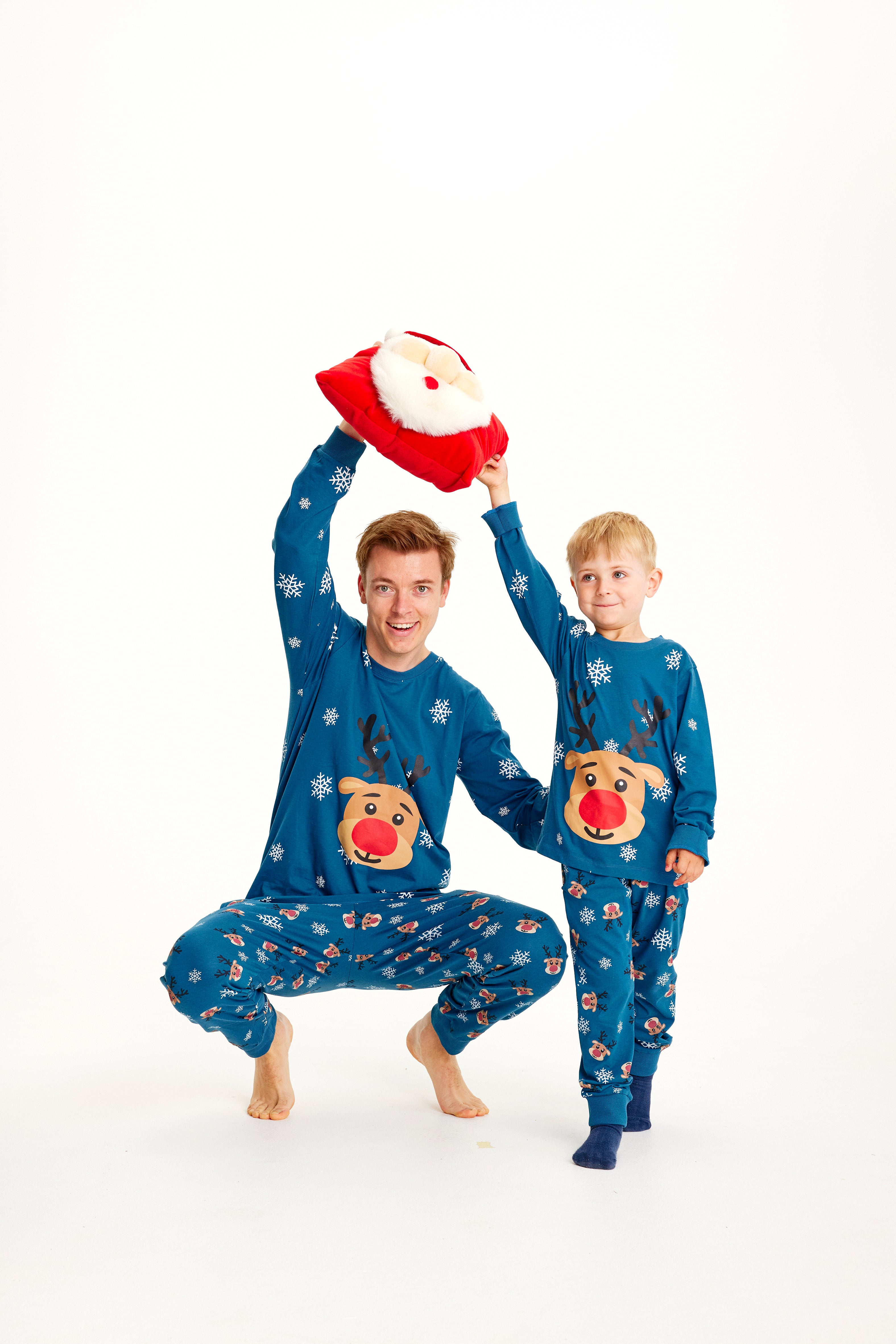 Et smilende barn og en mann i blå julepyjamas med reinsdyr og snøfnugg.